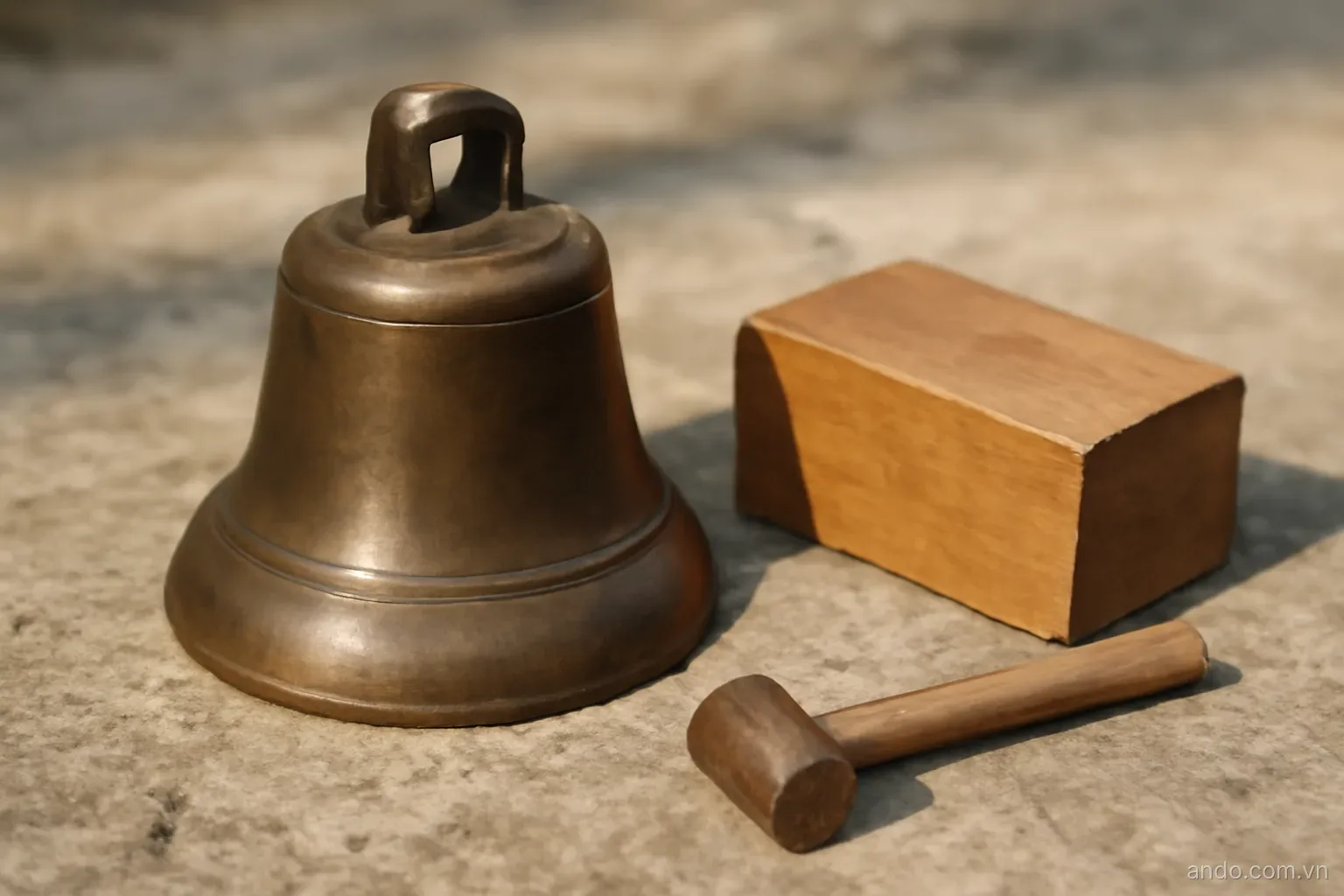 A bronze bell and a wooden block resting on a stone surface, one small mallet lying beside them, no text
