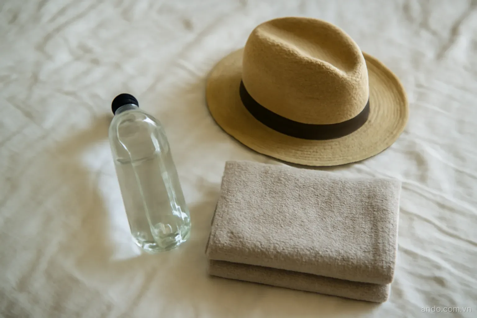 A small travel kit with a water bottle, a hat and a folded towel on a bed, top-down view, no text