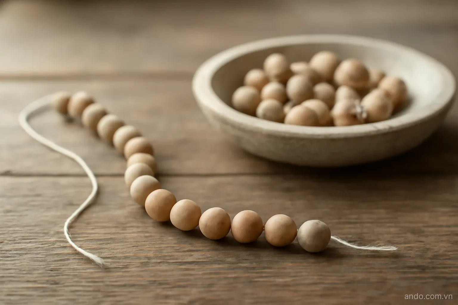 A partly threaded string of beads with the remaining beads waiting in a shallow stone dish, no text